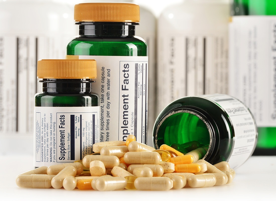 Dietary Supplement Insurance - Closeup View of Various Dietary Supplement Bottles on a White Background with Multi Colored Gold Pills Spilled Out of One Bottle on a Table