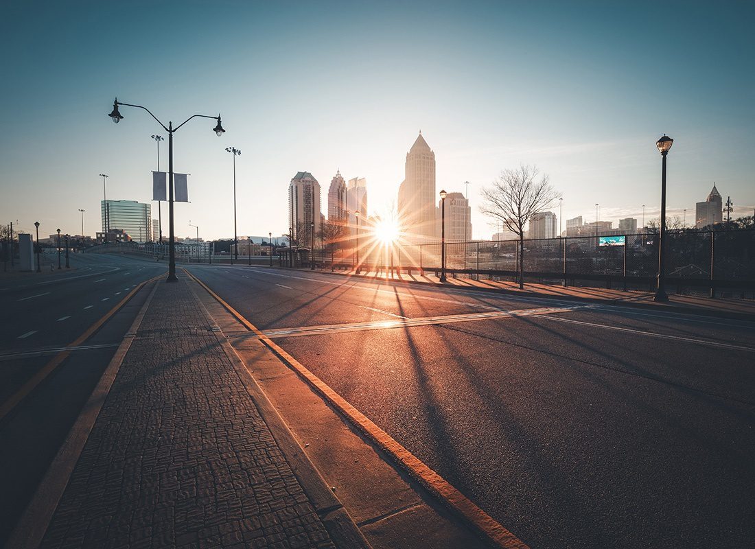 Insurance Solutions - View of an Empty Street in the City at Sunset with Views of Modern Commercial Buildings in the Background with the Sun Shining Through