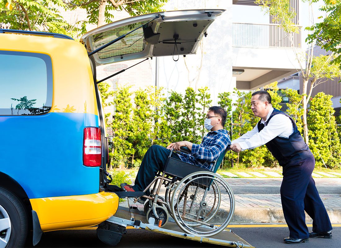 Non-Emergency Medical Transportation Insurance - Mature Driver Pushing a Young Man in a Wheelchair with a Mask into the Back of a Taxi Van