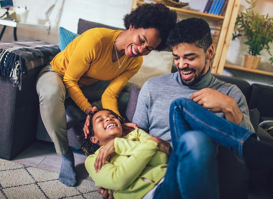 Personal Insurance - Portrait of Cheerful Parents Having Fun Playing with Their Laughing Daughter at Home in the Living Room